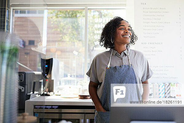 Smiling female owner with hands in pockets of apron at coffee shop