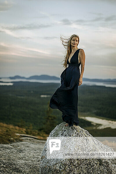 Blonde woman in long dark dress stands on rock. windblown.
