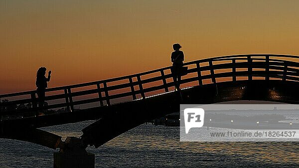 Dusk  sunset  wooden bridge  footbridge over canal  silhouette  pedestrians  one woman photographing other woman  Lefkada town  capital  Lefkada island  Lefkas  Ionian Islands  Greece  Europe