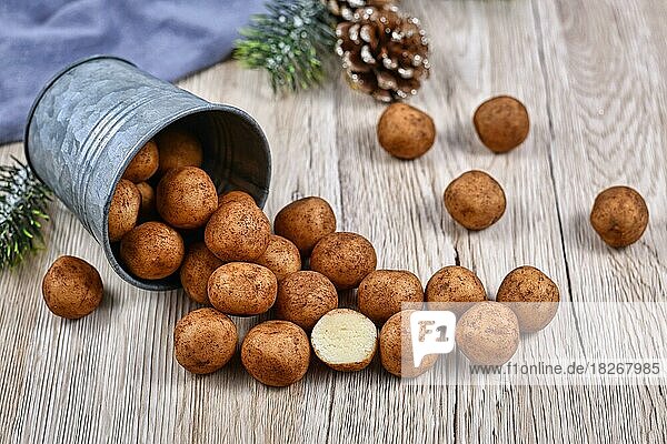 Traditionelle deutsche Weihnachtssüßigkeiten  genannt Marzipankartoffeln. Runde  kugelförmige  mit Zimt und Kakaopulver bestreute Mandelpastetchen  die aus einem Eisenbecher auf Holzuntergrund quellen