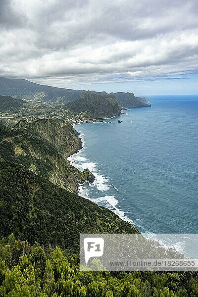 Ausblick auf steile bewaldete Küste und Meer  hinten Ort Porto da Cruz und Adlerfelsen Penha de Aguia  Küstenlandschaft  Wanderweg Vereda do Larano  Madeira  Portugal  Europa