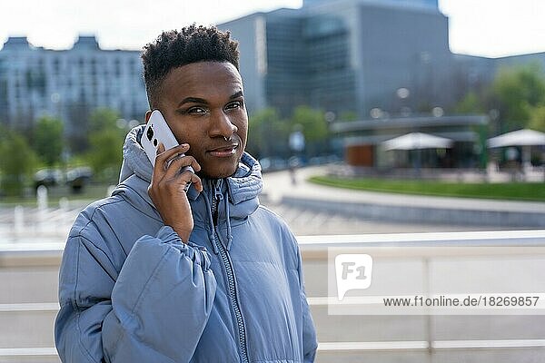 A black ethnic man with a phone and a blue jacket in the city  talking on the phone