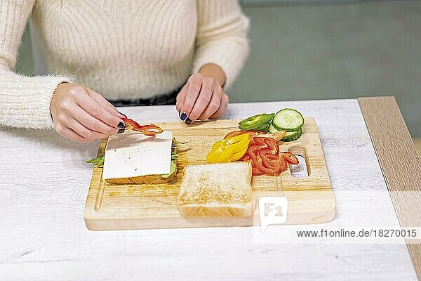 Unbekannte Person  die zu Hause in der Küche ein Gemüsesandwich zubereitet. Platzieren der roten Paprika