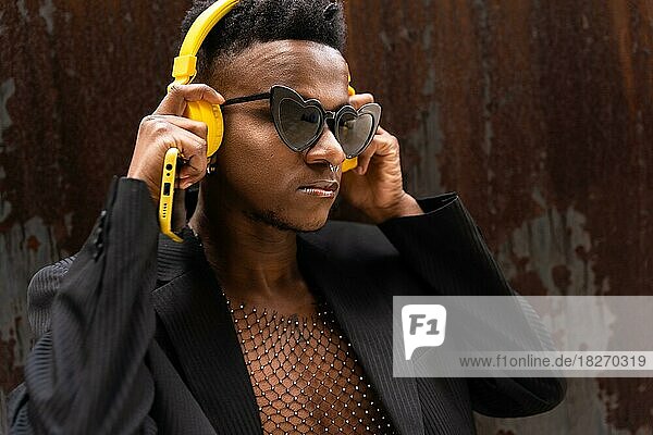 Ein schwarzer ethnischer Mann hört Musik über drahtlose gelbe Kopfhörer und trägt eine Herz-Sonnenbrille
