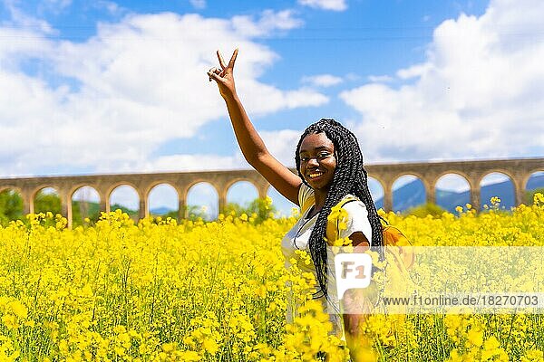 Das Siegeszeichen  ein schwarzes ethnisches Mädchen mit Zöpfen  eine Reisende  in einem Feld mit gelben Blumen