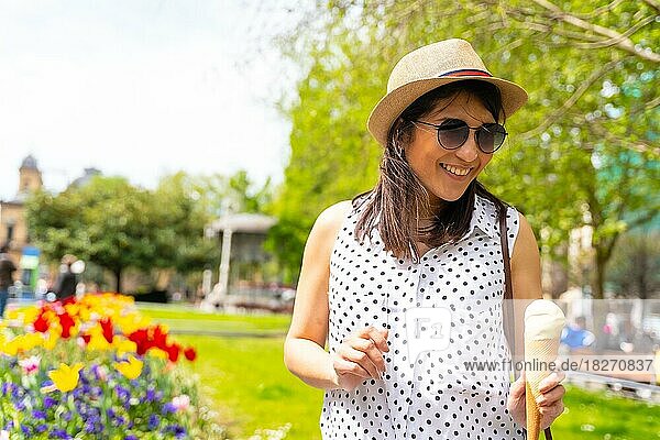 Eine touristische Frau  die die Stadt besucht  isst eine Eistüte  lächelt und genießt den Urlaub  Solo weibliche Reisende Konzept  trägt eine Sonnenbrille und einen Hut