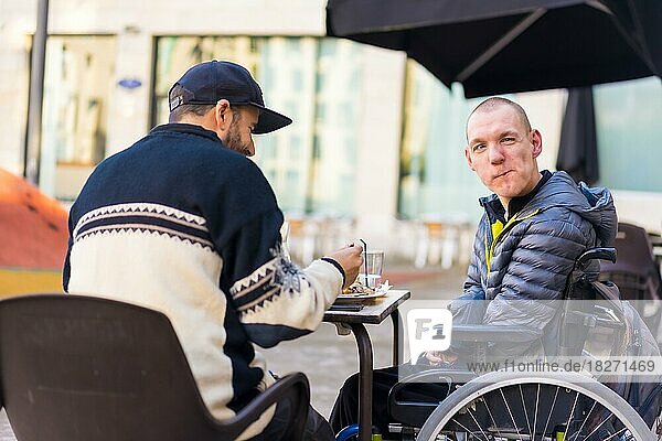 Freunde beim Essen auf der Terrasse eines Restaurants  behinderte Person  Rollstuhl