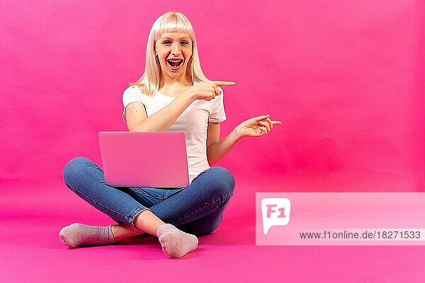 Blondes kaukasisches Mädchen mit einem Computer  Studioaufnahme auf rosa Hintergrund  Kopierraum  zeigend