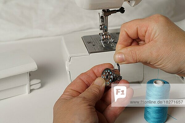 Nahaufnahme von Frauenhänden  die blauen Faden auf eine Nähmaschine legen