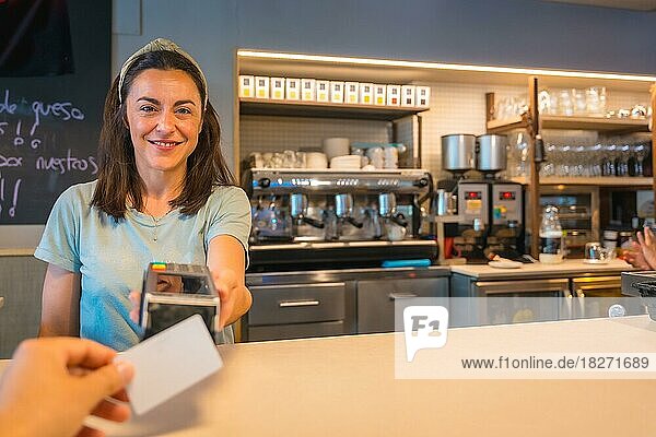 Eine brünette kaukasische Kellnerin  die lächelnd das Datentelefon übergibt  um mit dem Kreditkartenkontakt des Kunden aufzuladen