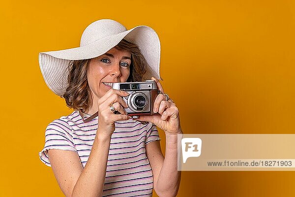 Kaukasisches Mädchen in touristischem Konzept mit Hut  das ein Foto macht und den Sommerurlaub genießt  gelber Hintergrund