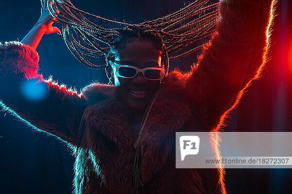 Schwarze ethnische Frau mit Zöpfen mit blauen und roten Lichtern  die Spaß haben und auf einer Party tanzen