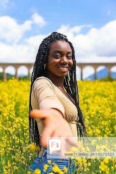 Lifestyle  die Hand anbieten  Porträt eines schwarzen ethnischen Mädchens mit Zöpfen  Reisende  in einem Feld von gelben Blumen
