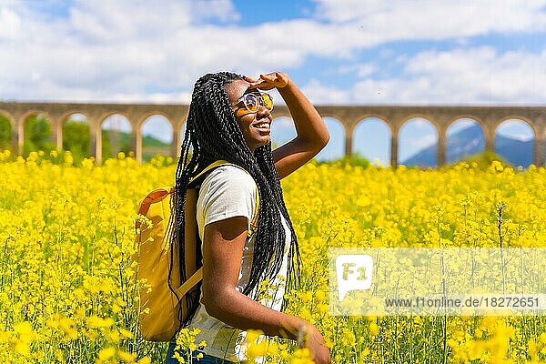 Porträt eines schwarzen ethnischen Mädchens mit Zöpfen  das in die Sonne schaut  Sonnenbrille  Reisende  in einem Feld mit gelben Blumen