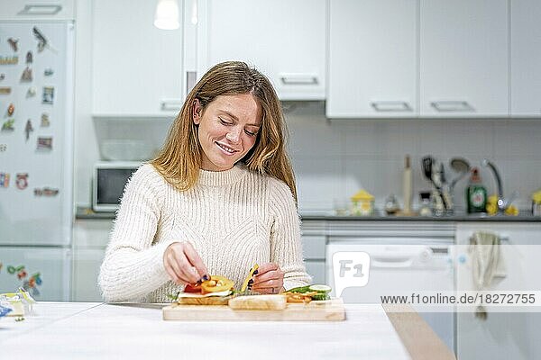 Vegetarische Frau beim Zubereiten eines Gemüsesandwiches in der Küche zu Hause. Sie bereitet es vor  indem sie die Tomate