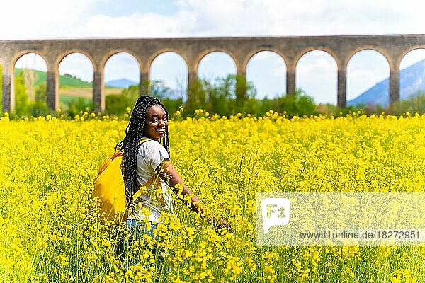 Ein Mädchen schwarzer Herkunft mit Zöpfen  eine Reisende  die in einem Feld mit gelben Blumen spazieren geht