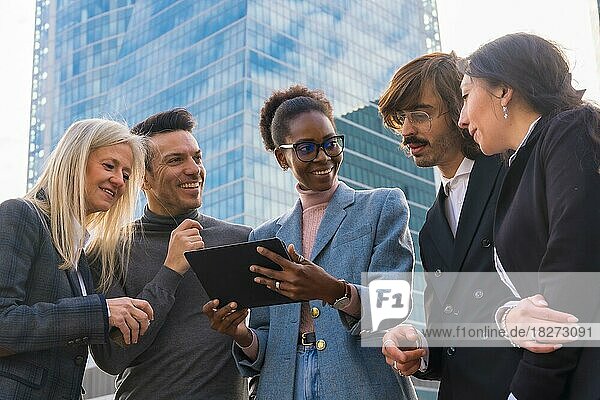 Gruppe lächelnder multiethnischer Geschäftsleute  die vor einem gläsernen Bürogebäude auf eine Tafel schauen