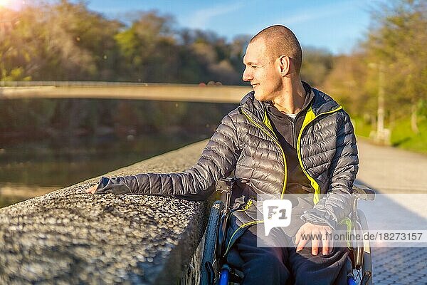 Eine behinderte Person in einem Rollstuhl in einem Park bei Sonnenuntergang neben einem Fluss bei Sonnenuntergang