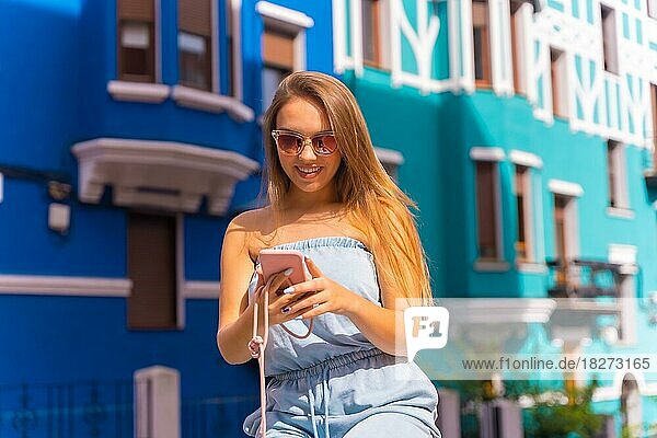 Junge attraktive blonde Touristin schaut auf das Handy  hinter bunter gelber und grüner Fassade