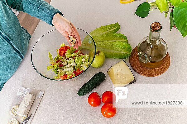 Frau  die an ihrem Küchentisch Cashewnüsse zu einem gesunden Salat hinzufügt