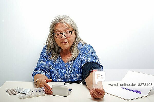 Ältere weißhaarige Frau mit Brille  die zu Hause ihren Blutdruck misst  mit weißem Hintergrund