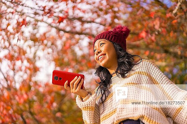 Porträt einer asiatischen Frau im Herbst mit einem Handy  die eine Sprachnachricht in einem Wald aus roten Blättern sendet  Technik