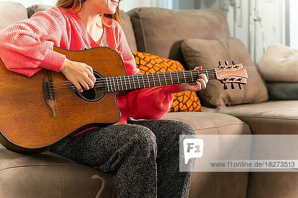 Gitarre spielen zu Hause auf dem Sofa in ihrem Wohnzimmer neben dem Verkauf