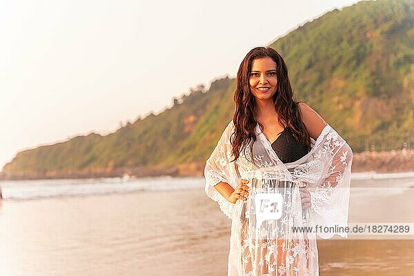 Porträt einer Frau bei Sonnenuntergang in einem weißen Kleid  die den Sommer am Strand genießt