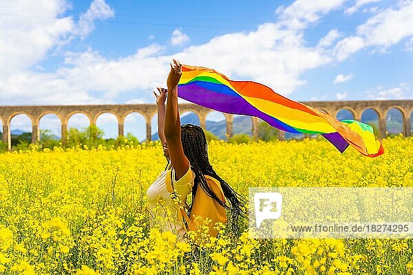 Eine schwarze ethnische Mädchen mit Zöpfen hält die LGBT-Flagge in einem Feld von gelben Blumen  Stolz Tag  freie Frauen Konzept