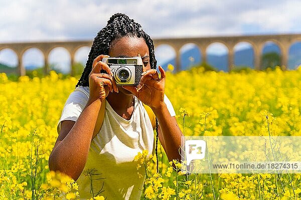 Fotografieren mit einer alten Kamera  ein schwarzes ethnisches Mädchen mit Zöpfen  eine Reisende  in einem Feld mit gelben Blumen