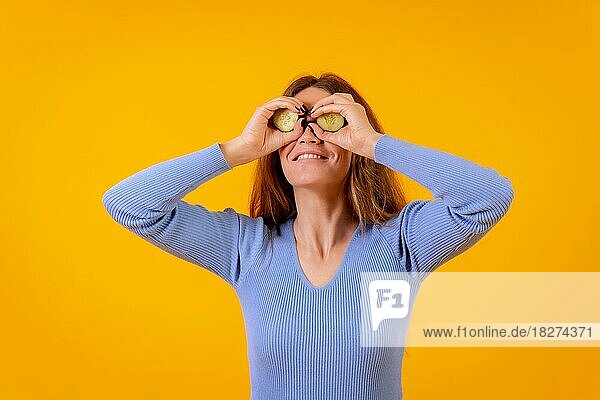Vegane Frau mit Gurkenscheiben auf ihren Augen auf einem gelben Hintergrund  vegetarisches Leben