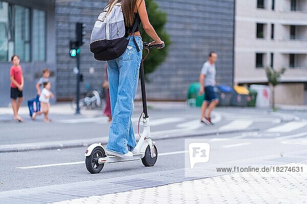 Eine junge brünette Frau  die sich mit einem Elektroroller in der Stadt bewegt  auf dem Fahrradweg in Richtung Universität