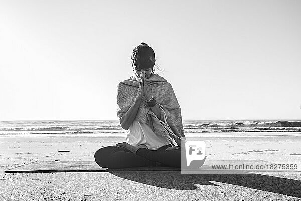 Porträt einer Frau  die am Strand eine Japa Mala in den Händen hält. Namaste-Pose. Vorderansicht