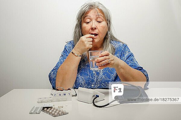 Ältere weißhaarige Frau  die eine Tablette einnimmt  nachdem sie ihren Blutdruck überprüfen ließ