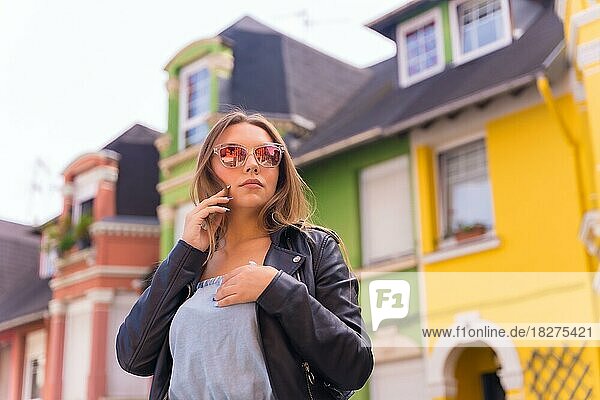 Attraktive junge blonde Frau in Lederjacke und Sonnenbrille lächelnd  hinter bunter Fassade