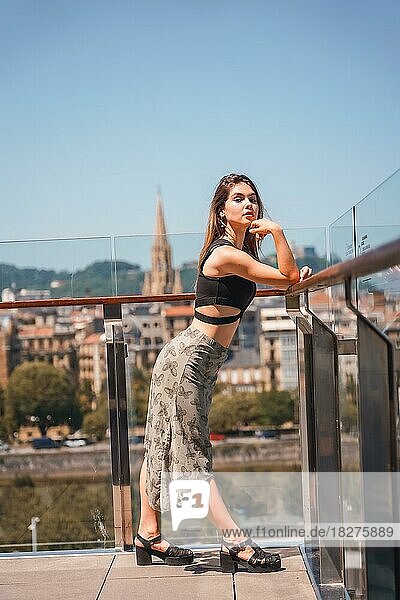 Posing of a young woman on the terrace of a hotel looking at the city from above  glass railing