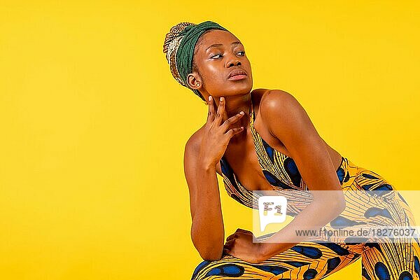 Eine weibliche Person schwarzer Ethnizität mit traditioneller Tracht auf gelbem Hintergrund  in Mode posiert