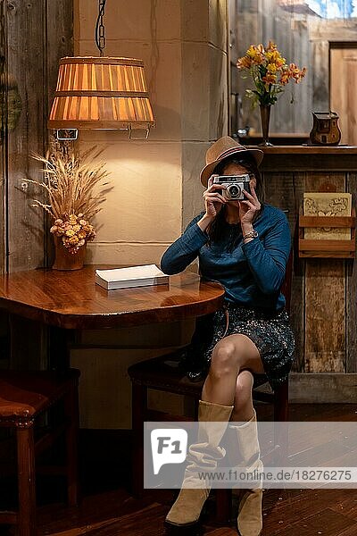 Eine hübsche Touristin mit Hut und Fotoapparat trinkt Tee in einem Café und macht ein paar Fotos mit der alten Kamera