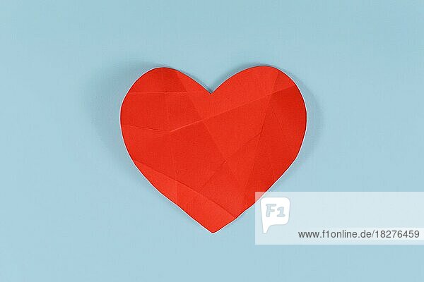Gebrochenes rotes Papierherz mit Faltlinien auf blauem Hintergrund. Konzept für gebrochenes oder krankes Herz