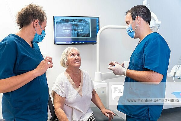 Zahnklinik  Zahnarzt und Assistentin erklären einer älteren Frau eine Zahnbehandlung  Zahnersatz