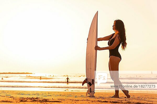 Porträt einer Surferin am Strand bei Sonnenuntergang mit dem Surfbrett