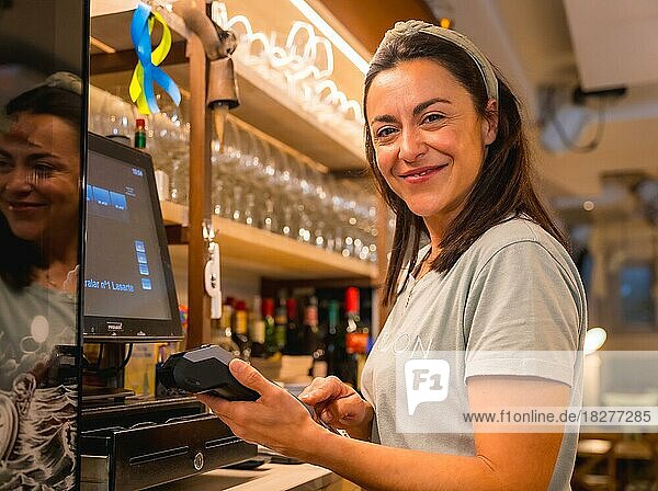 Brunette caucasian waitress cashing with card in coffee shop