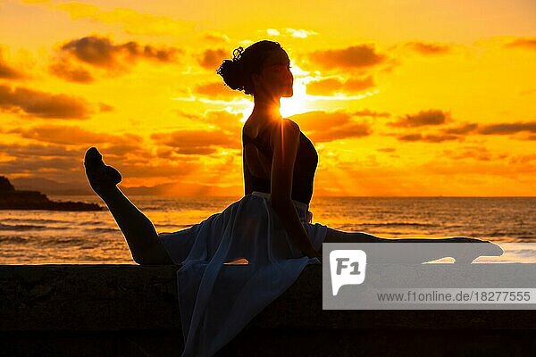 Eine junge Tänzerin am Strand bei Sonnenuntergang macht Spagata mit dem Meer im Hintergrund