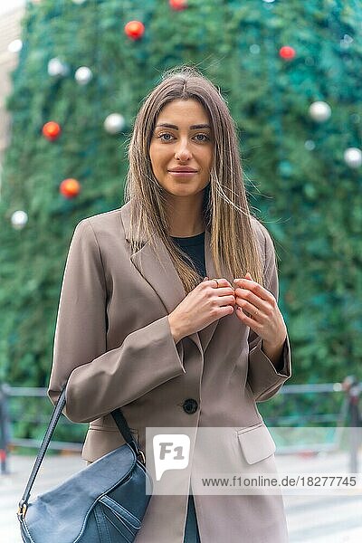 Weihnachtsbaum in der Stadt  junge Frau im Trenchcoat schaut in die Kamera