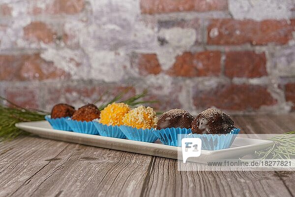 Süße Trüffel in verschiedenen Geschmacksrichtungen auf einem weißen Keramiktablett auf einem Holztisch