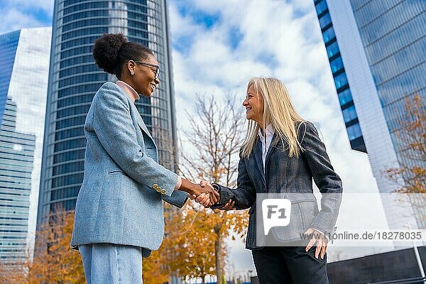 Multiethnische Geschäftsfrauen und Führungskräfte mittleren Alters  die sich in einem Gewerbegebiet per Handschlag begrüßen