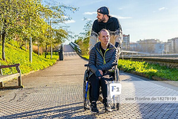 Lächelnde behinderte Person im Rollstuhl  die mit ihrem Bruder in einem Park spazieren geht