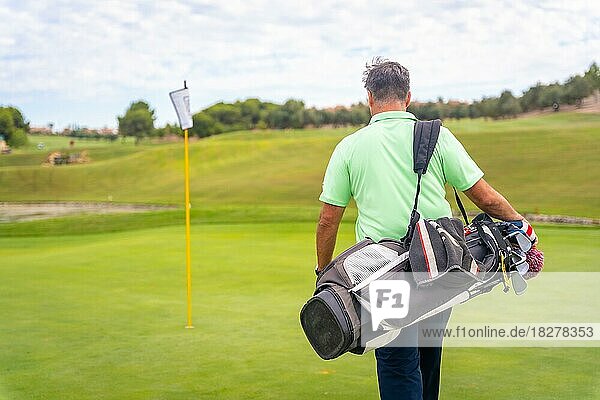 Porträt eines männlichen Golfspielers  der mit seinen Taschen das Fairway entlangläuft und Golf spielt