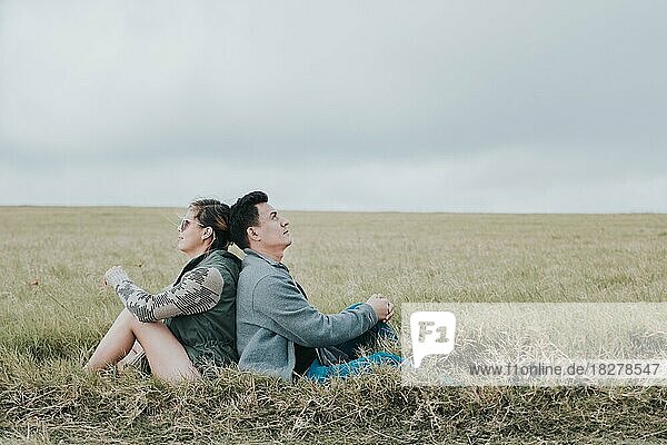 Verliebtes Paar auf dem Feld  Rücken an Rücken sitzend und in den Himmel blickend  Junges entspanntes Paar  das mit dem Rücken zueinander auf dem Feld sitzt und in den Himmel blickt