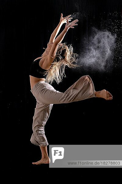 Junge Tänzerin  die einen Sprung auf einem schwarzen Hintergrund  Ballett  Einfrieren des Bildes mit Staub